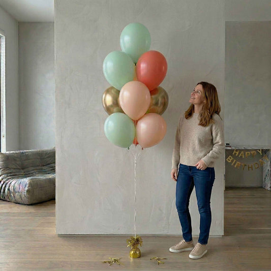 Woman holding a large bouquet of colorful balloons in a room with a 'Happy Birthday' banner.