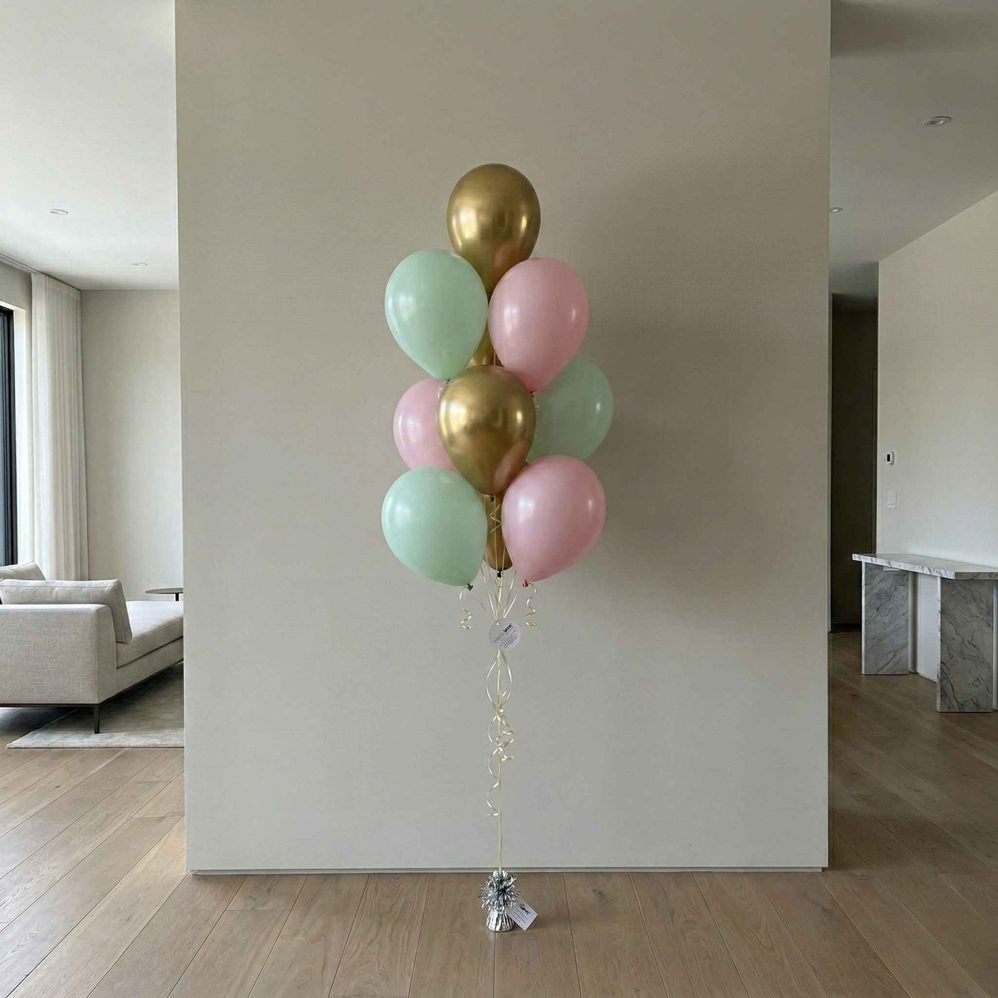 Bouquet of balloons in gold, pink, and green against a plain wall.