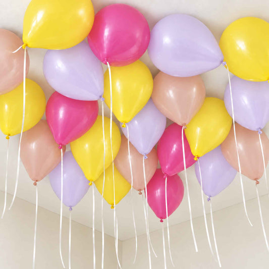A cluster of latex balloons in pastel yellow, pink, lavender, and blush pink, tied to a white ceiling with long white strings hanging down.