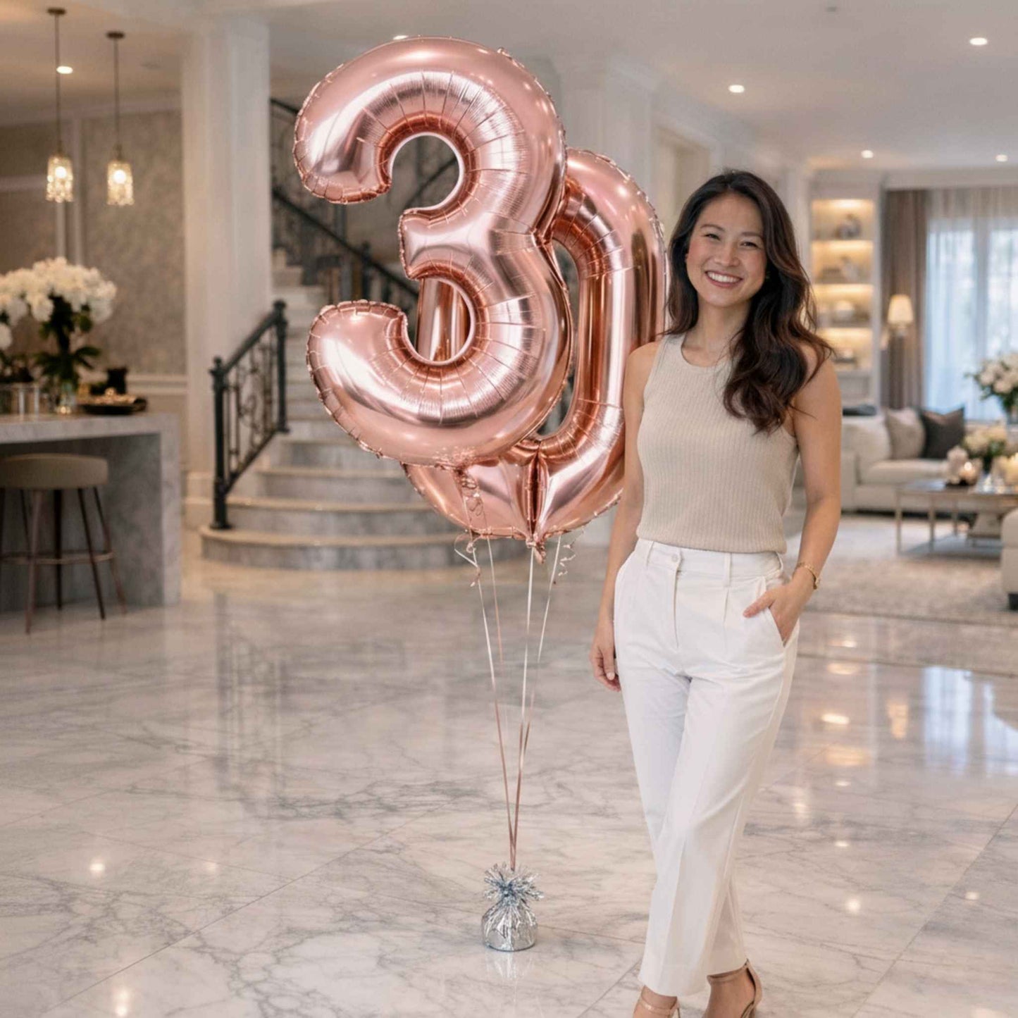Woman standing by rose gold number 3 and 0 foil balloons in a modern home setting