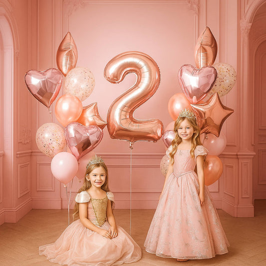 Two young girls in formal dresses standing in a room with pink balloons and a large number '2' balloon.