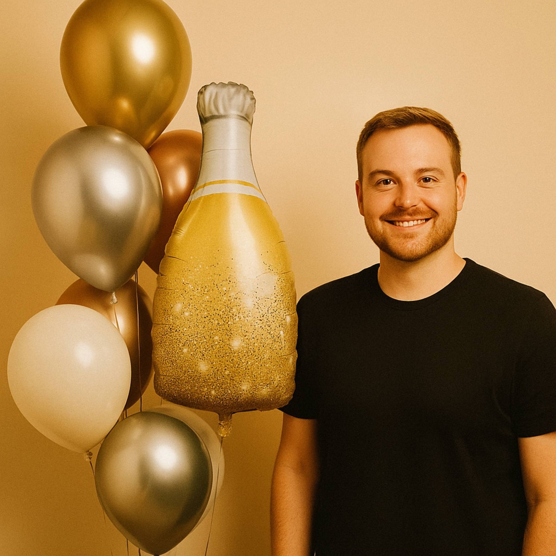 Man standing next to a large inflatable champagne bottle and balloons on a beige background