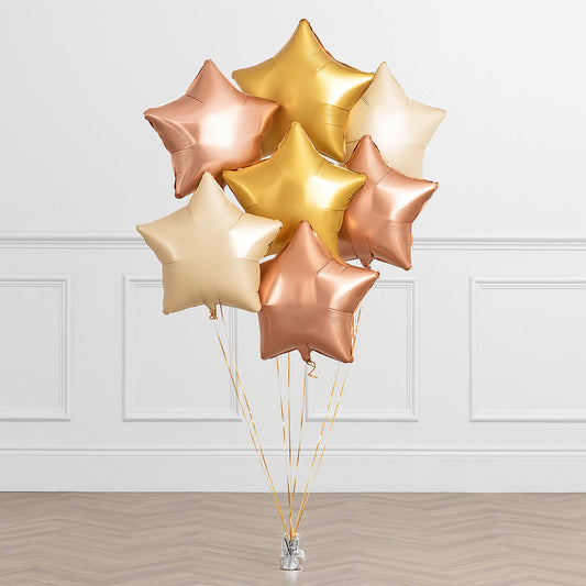 Bouquet of gold, rose gold, and white star-shaped balloons against a white paneled wall.