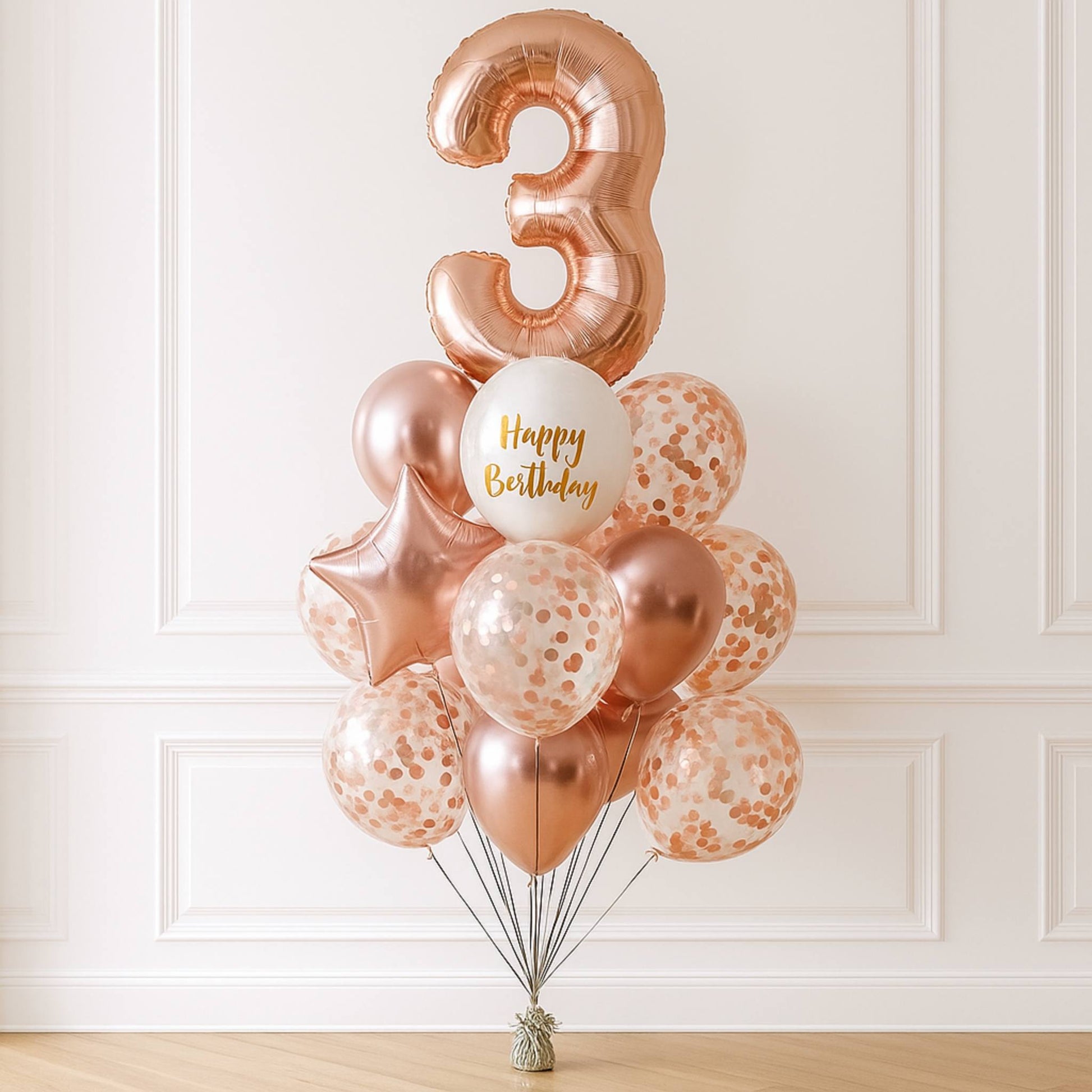 Rose gold balloons with a number 3 and 'Happy Birthday' balloon against a white wall.
