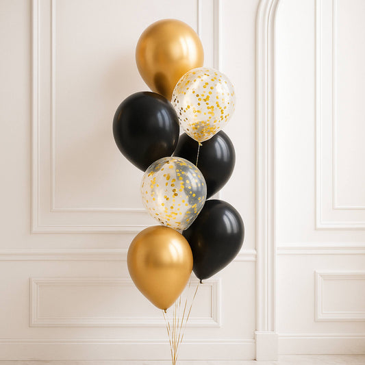 Bouquet of gold, black, and clear confetti balloons against a white wall.
