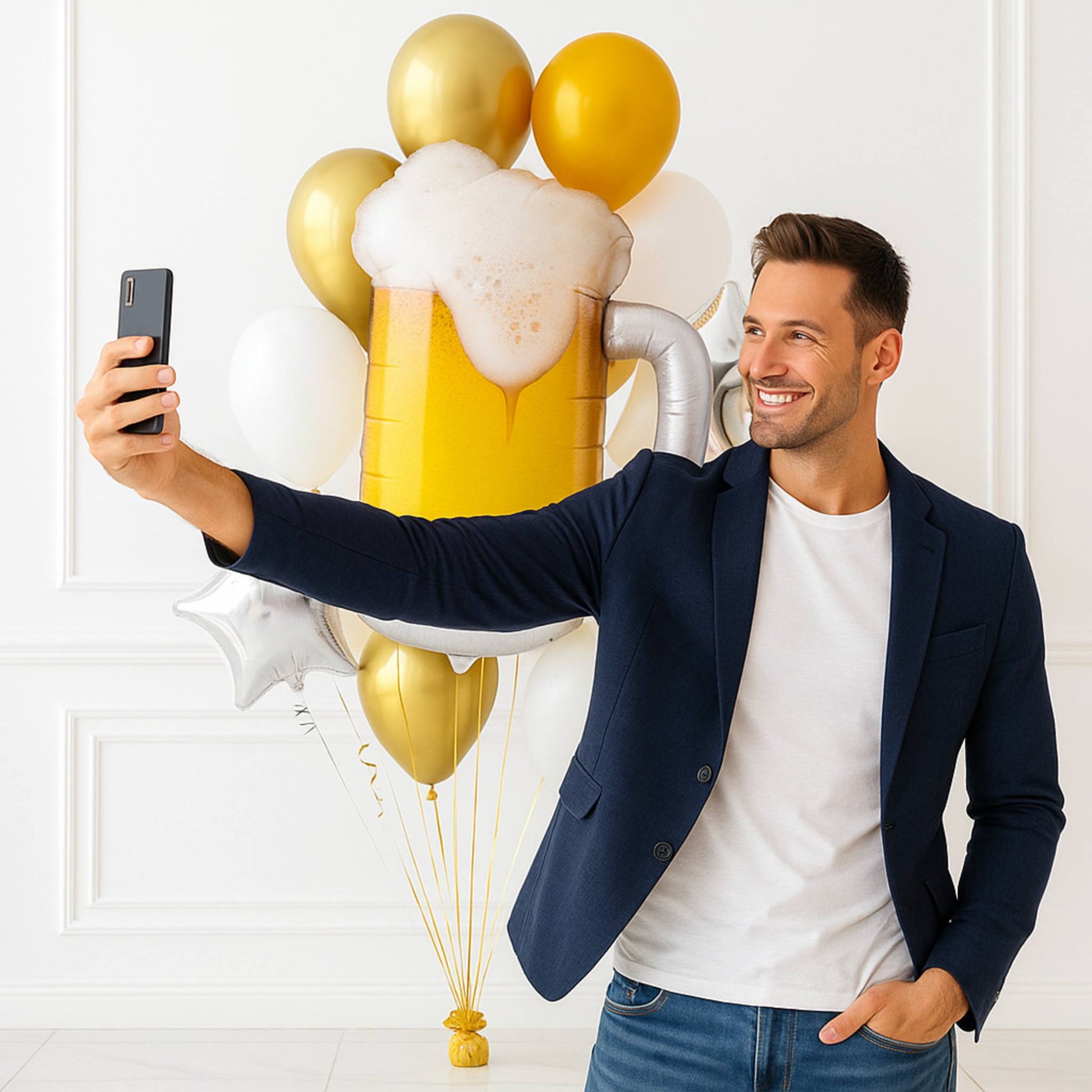 Man taking a selfie with a large inflatable beer glass and gold balloons against a white background