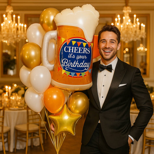 Man in a tuxedo holding a large inflatable beer mug with balloons in a celebratory setting.