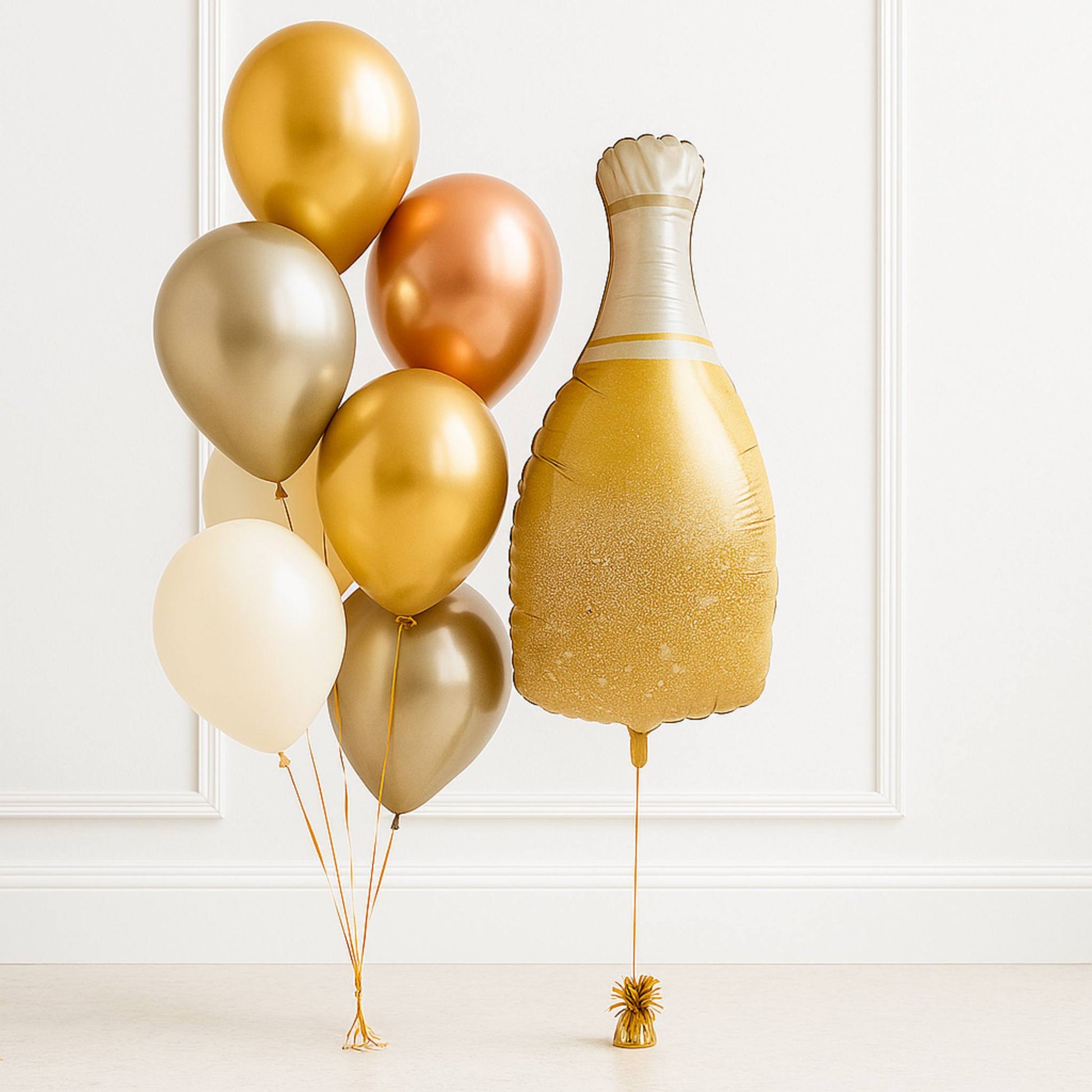 Gold champagne bottle balloon and other gold balloons against a white wall