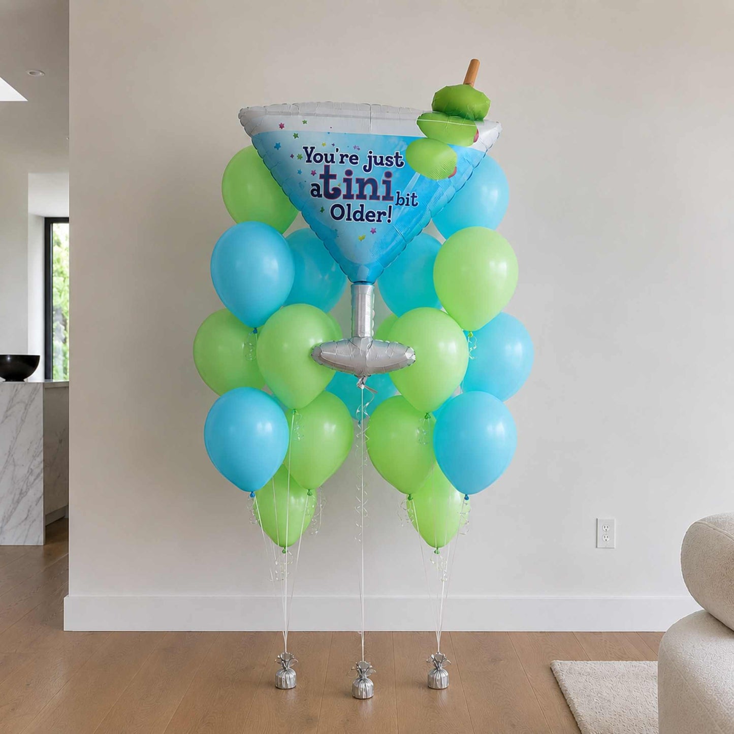 Decorative balloon stand with blue and green balloons and a cocktail glass-shaped balloon in a room.