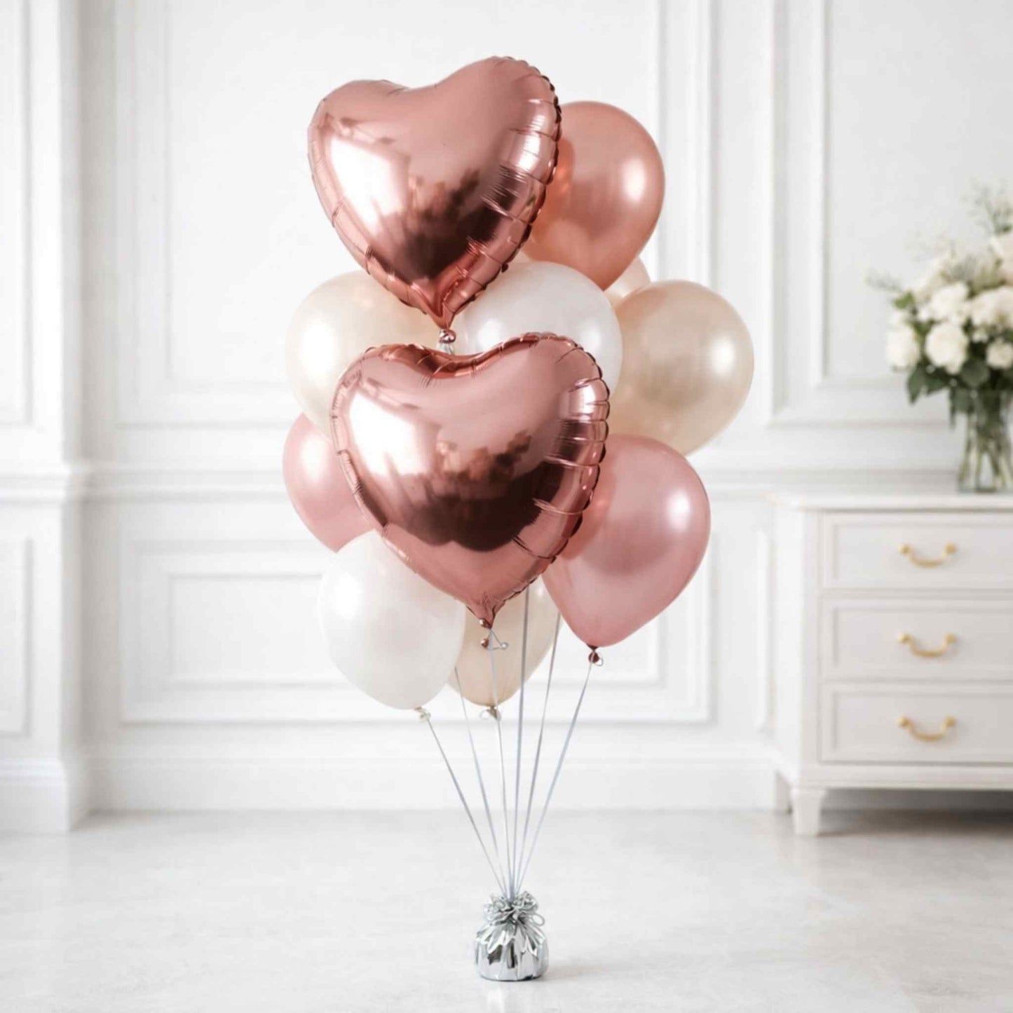 Rose gold heart-shaped balloons in a room with white walls and a dresser.