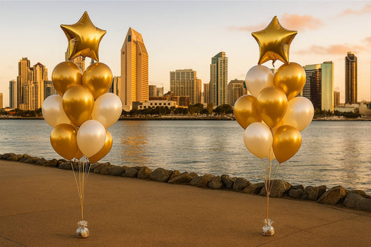 Gold and white balloons with star-shaped balloons against a city skyline and water backdrop.