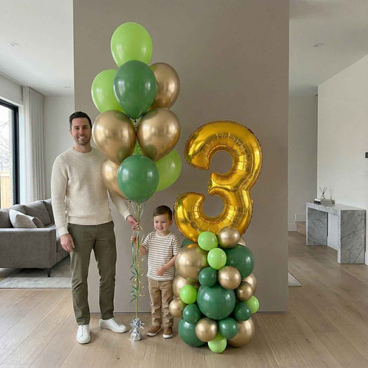 Man and child with green and gold balloons, including a large number three balloon, in a living room.