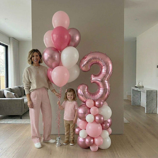 Woman and child with pink and white balloons, including a large number '3' balloon, in a home setting.