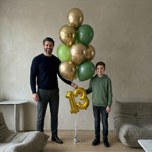 Man and kid holding balloons with a gold number 13 in a living room.