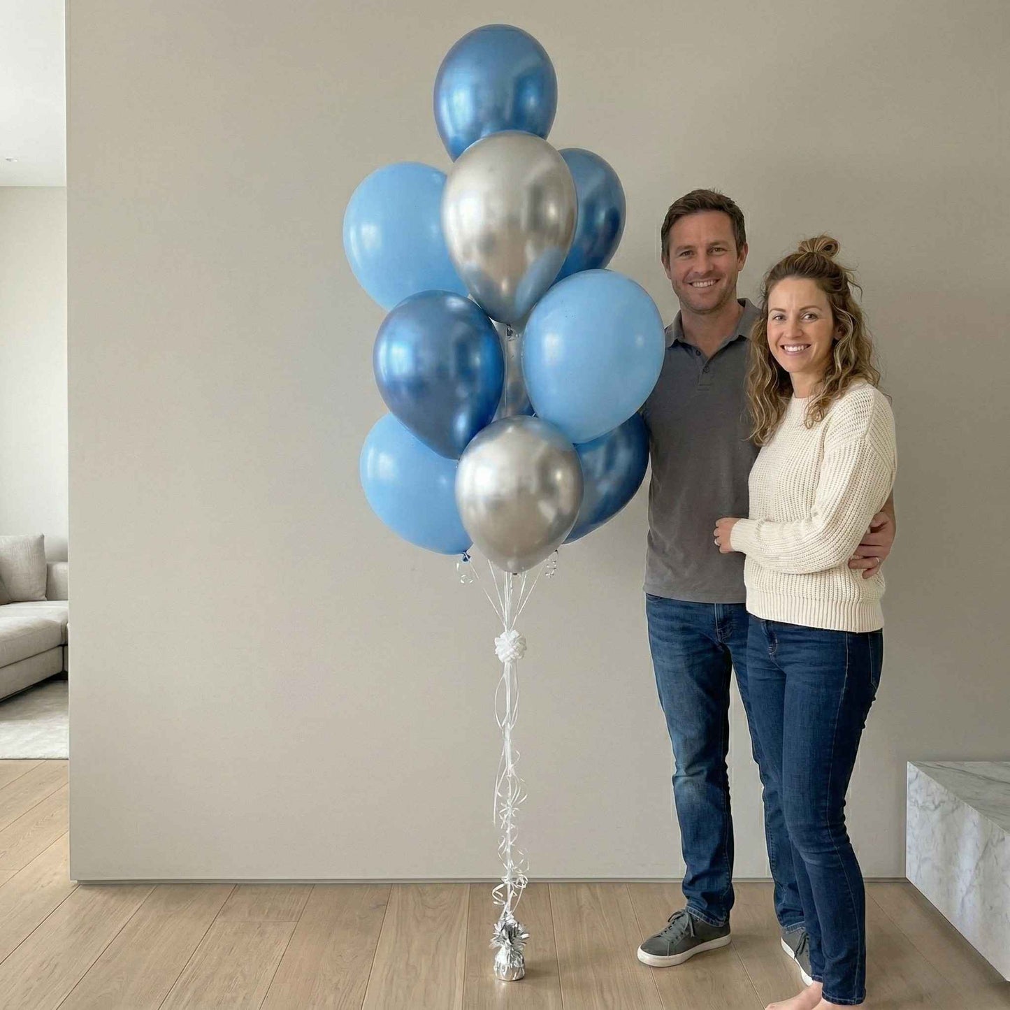 Man and woman standing indoors with a large bouquet of blue and silver balloons.