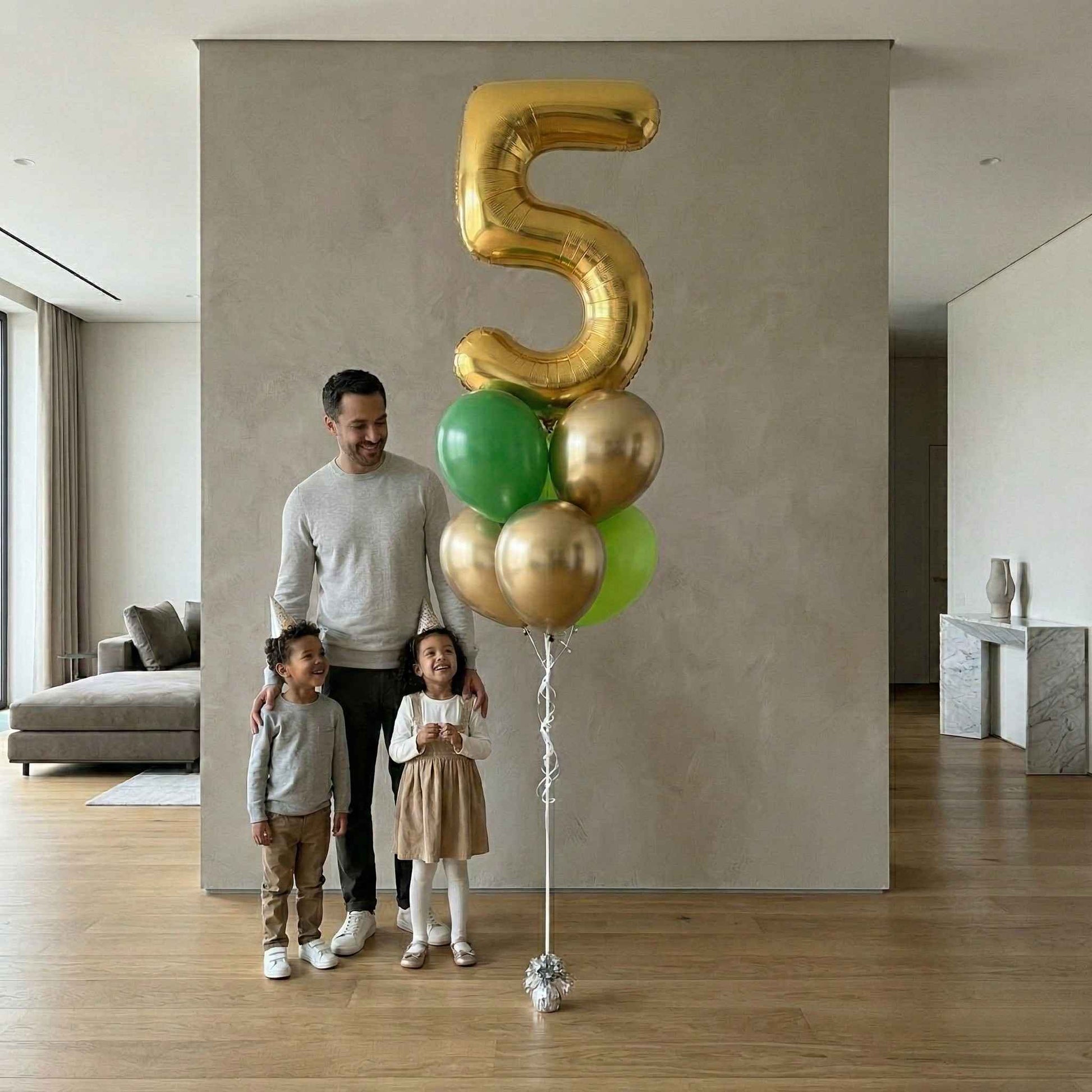 Man and two children standing next to a large gold number 5 balloon in a modern living room.