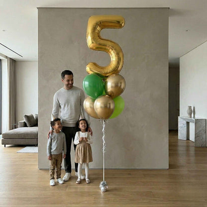 Man and two children standing next to a large gold number 5 balloon in a modern living room.