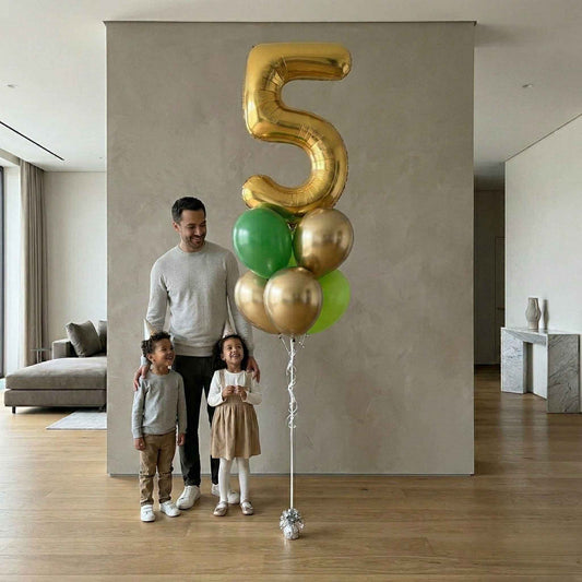 Man and two children standing next to a large gold number 5 balloon in a modern living room.