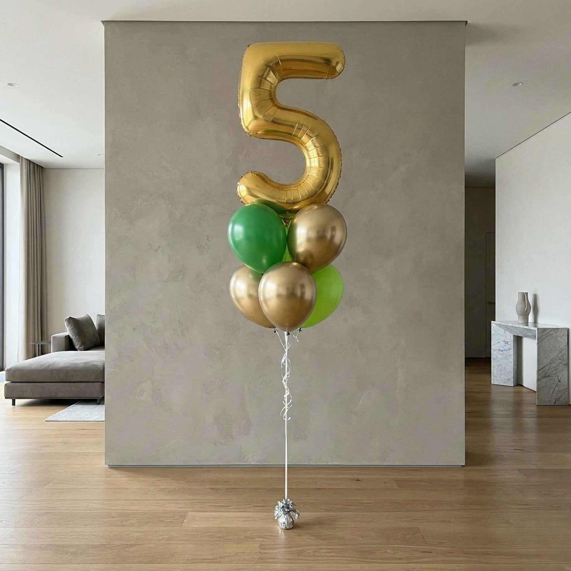 Gold and green balloons shaped like the number five in a modern living room.