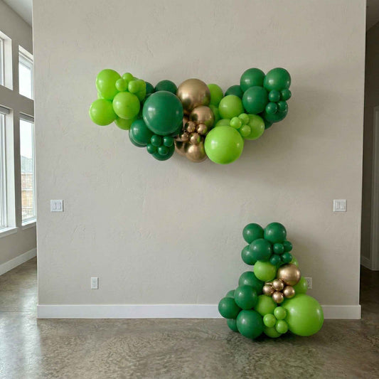 Green and gold balloon decorations on a plain wall