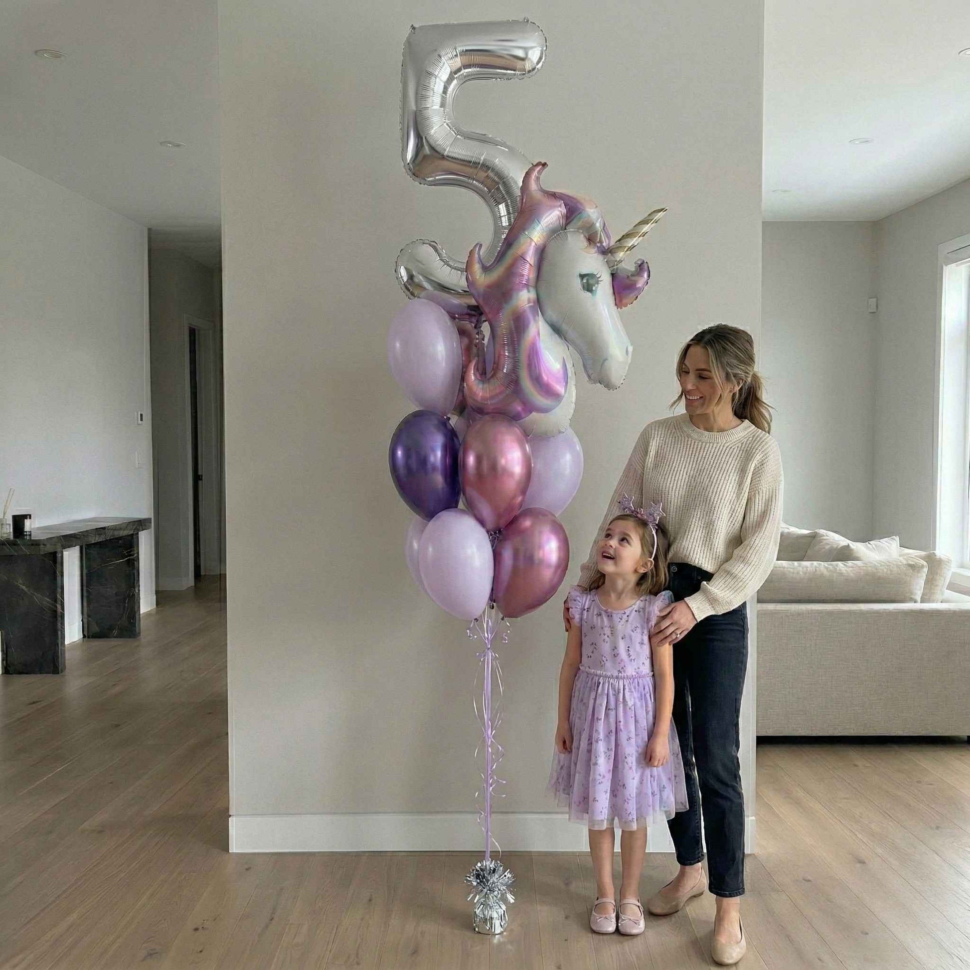 Woman and child standing next to a large unicorn-shaped balloon with number 5, in a living room setting.