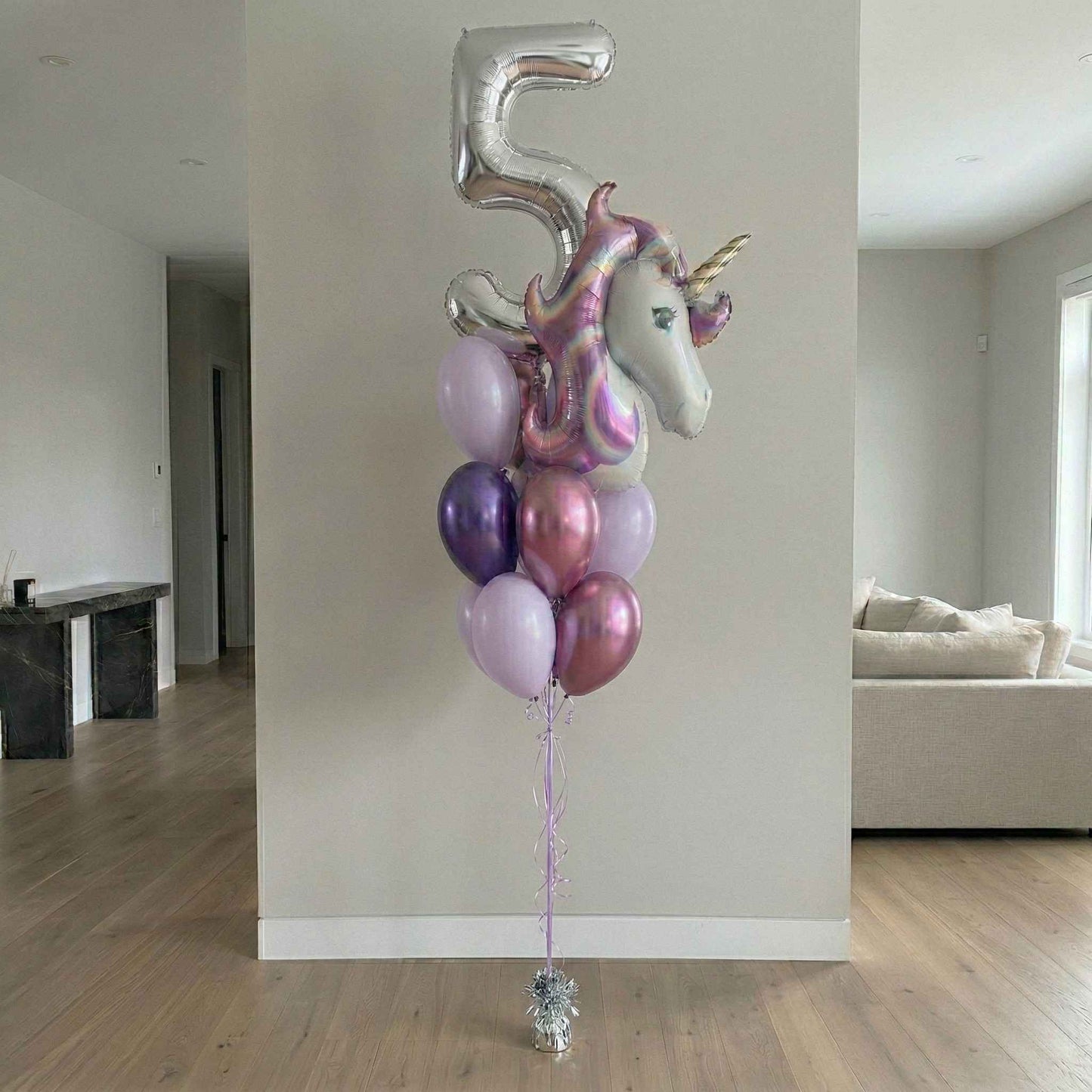 Unicorn-shaped balloon with number 5 against a neutral wall in a room.