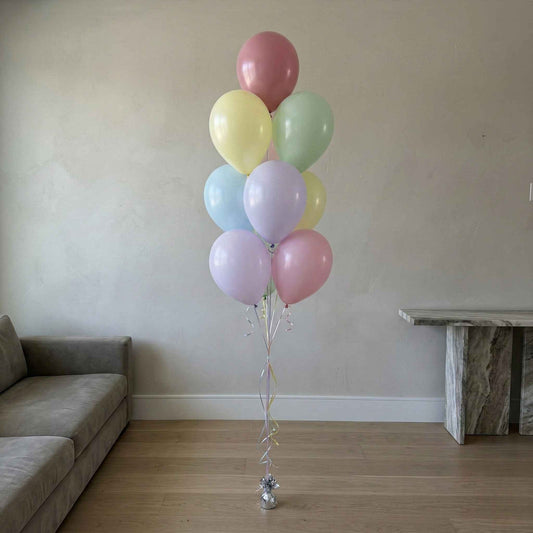 Bouquet of pastel balloons in a living room setting with a sofa and table.