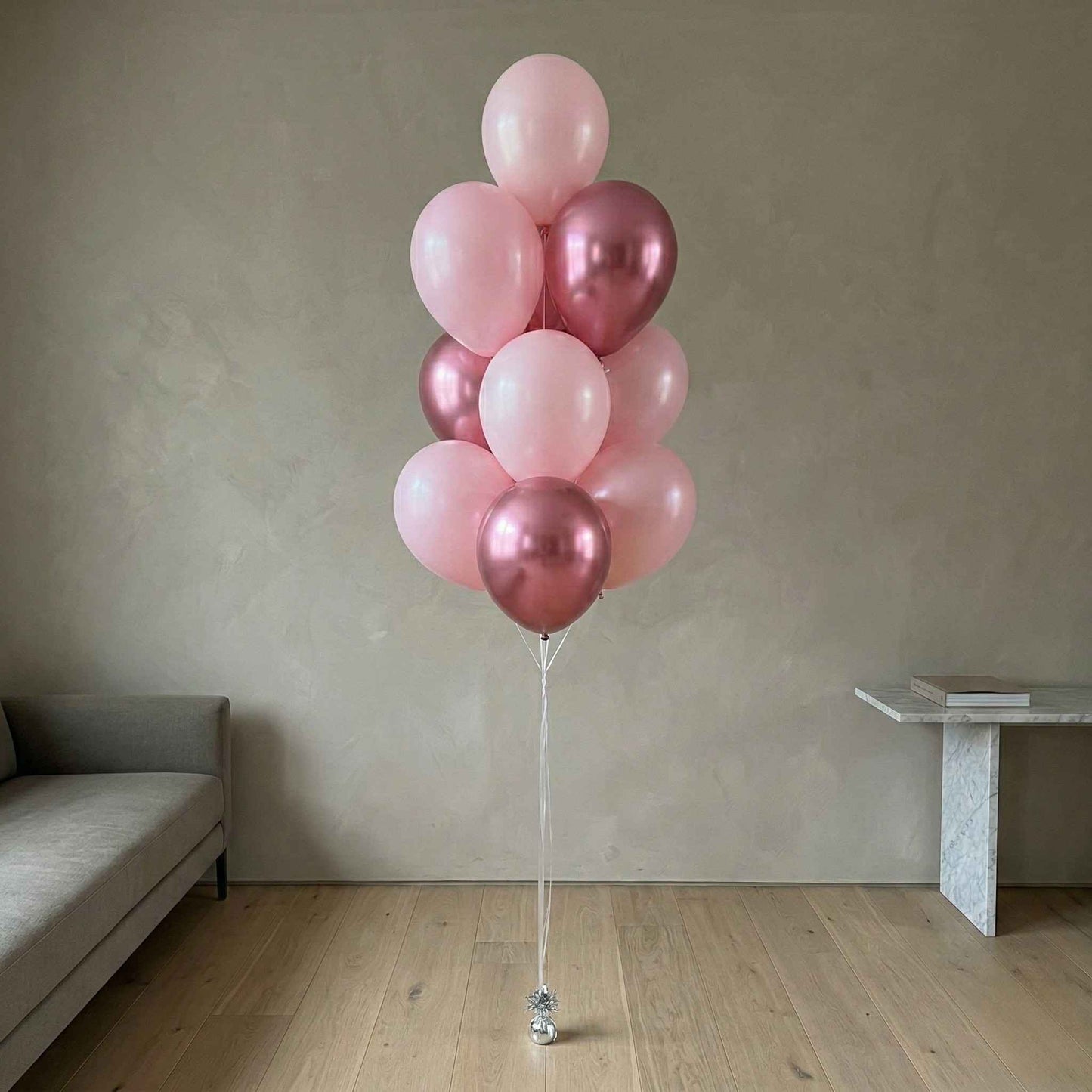 Bunch of pink and rose gold balloons on a stand in a room with a sofa and table.