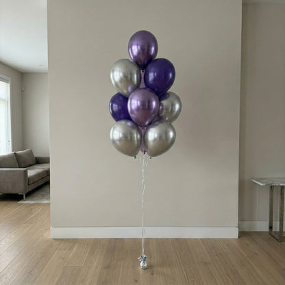 Bouquet of purple and silver balloons against a beige wall.