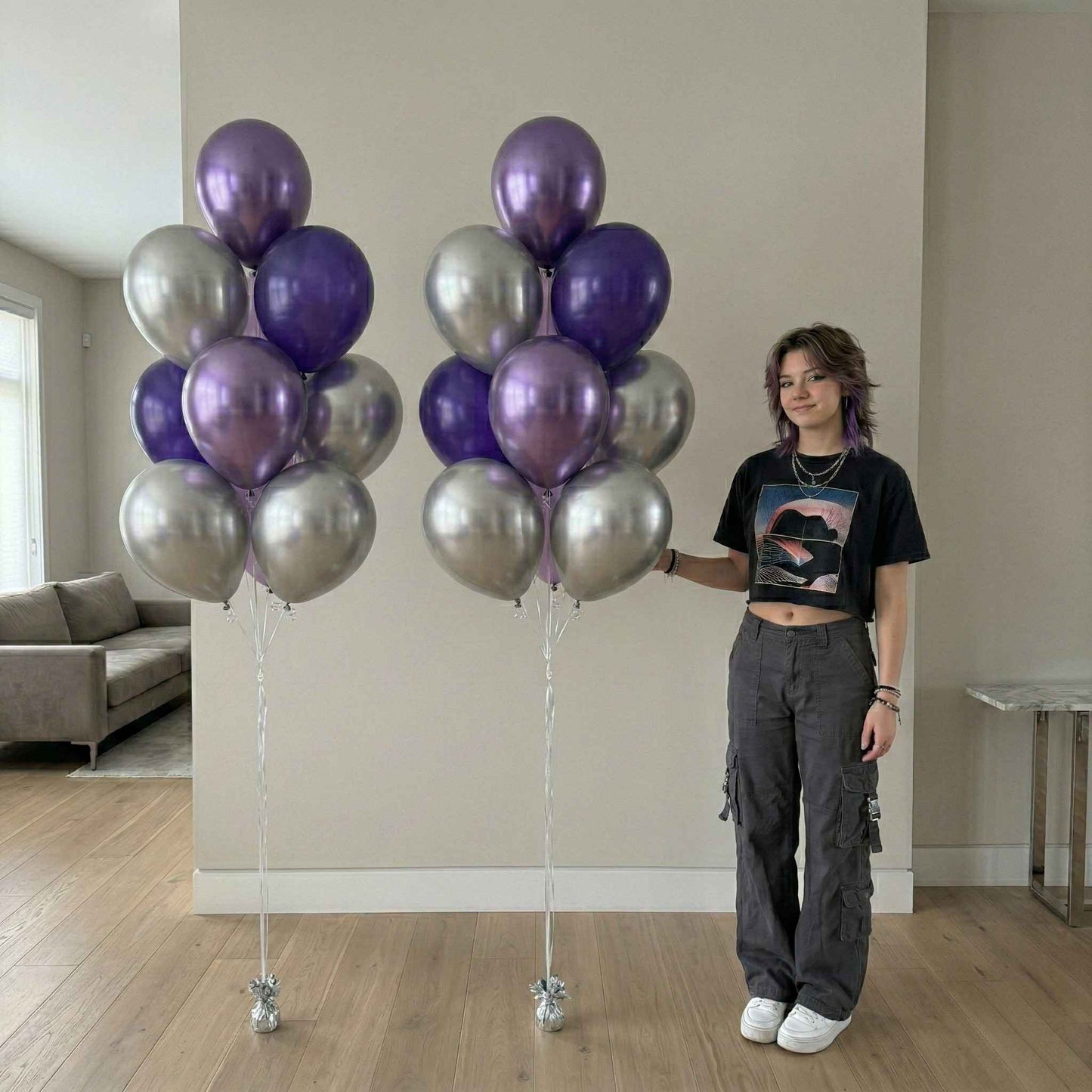 Person holding two large bunches of purple and silver balloons in a room.