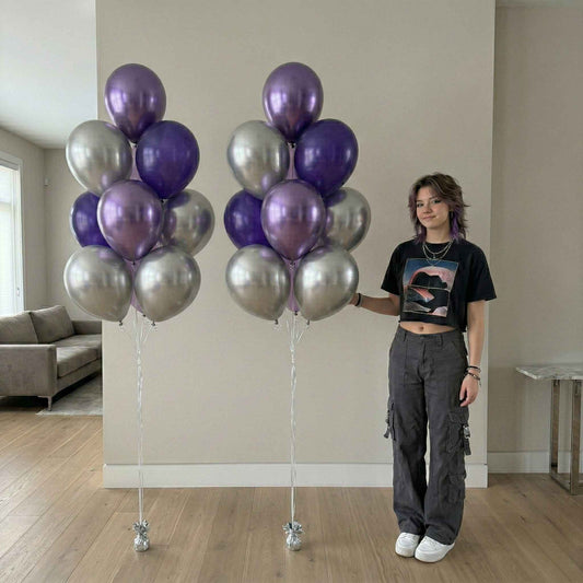 Person holding two large bunches of purple and silver balloons in a room.