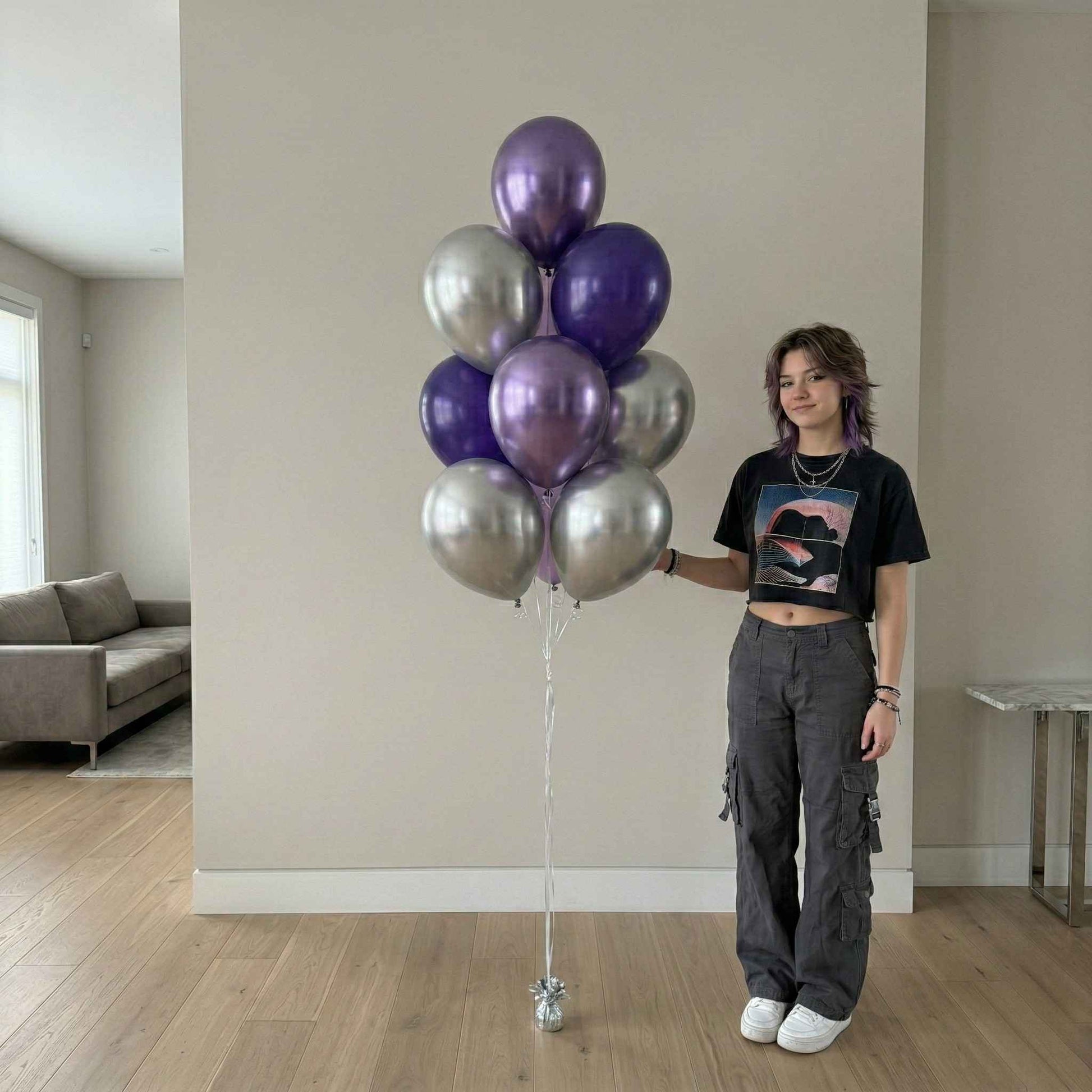 Person holding a bunch of purple and silver balloons in a room with a couch and table.