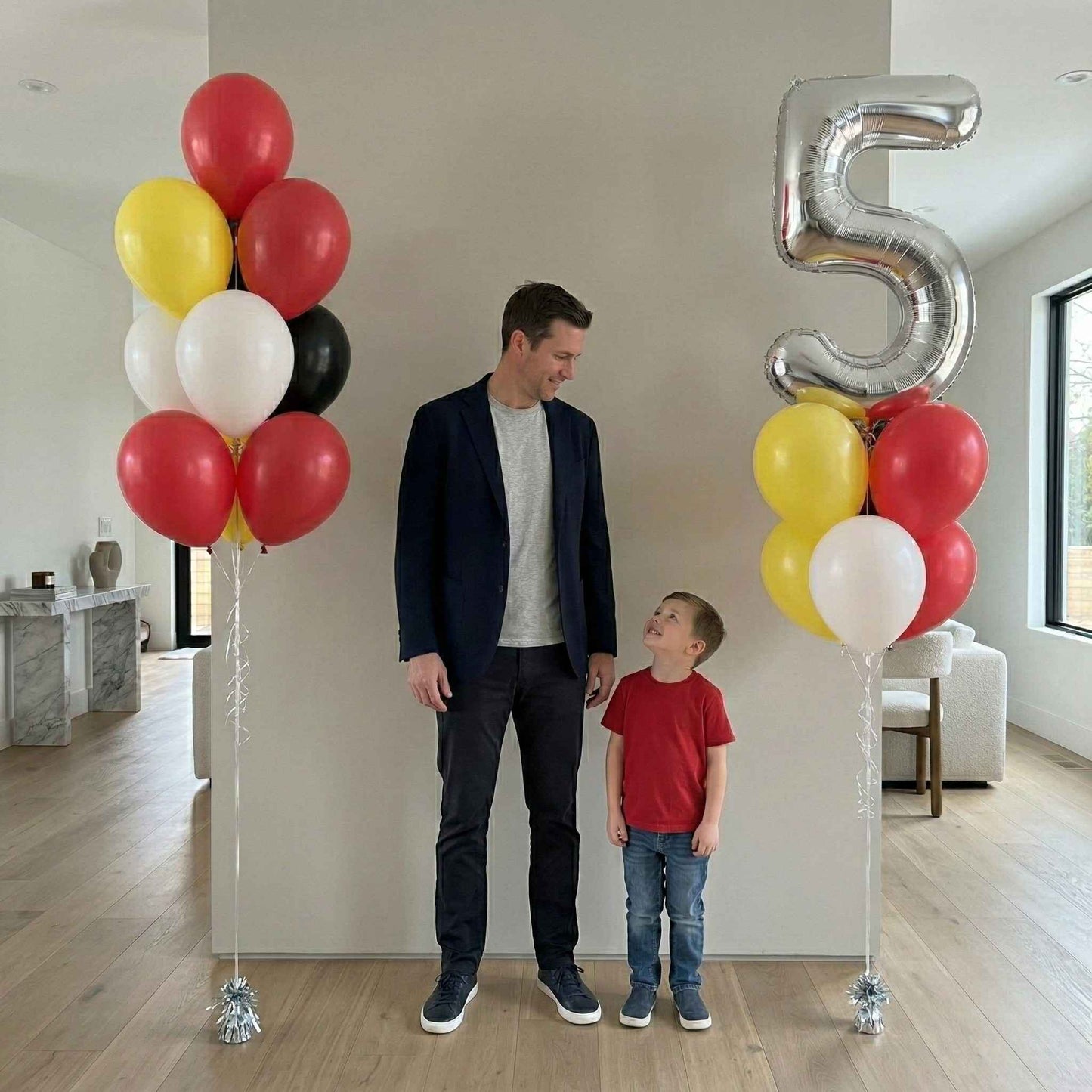 Man and child standing next to balloons and a large number 5 in a room.