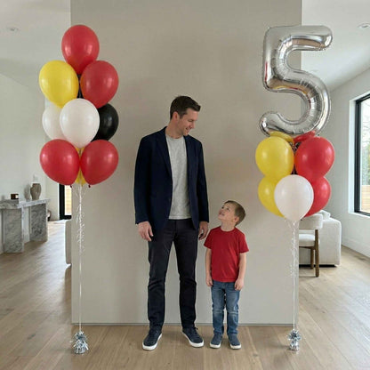 Man and child standing next to balloons and a large number 5 in a room.