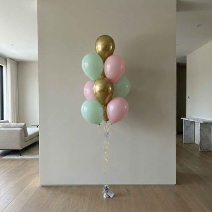 Bouquet of balloons in gold, pink, and green against a plain wall.