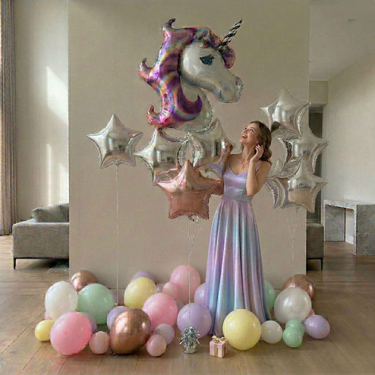 Woman in a long, light-colored dress holding a unicorn-shaped balloon in a room with colorful balloons on the floor.