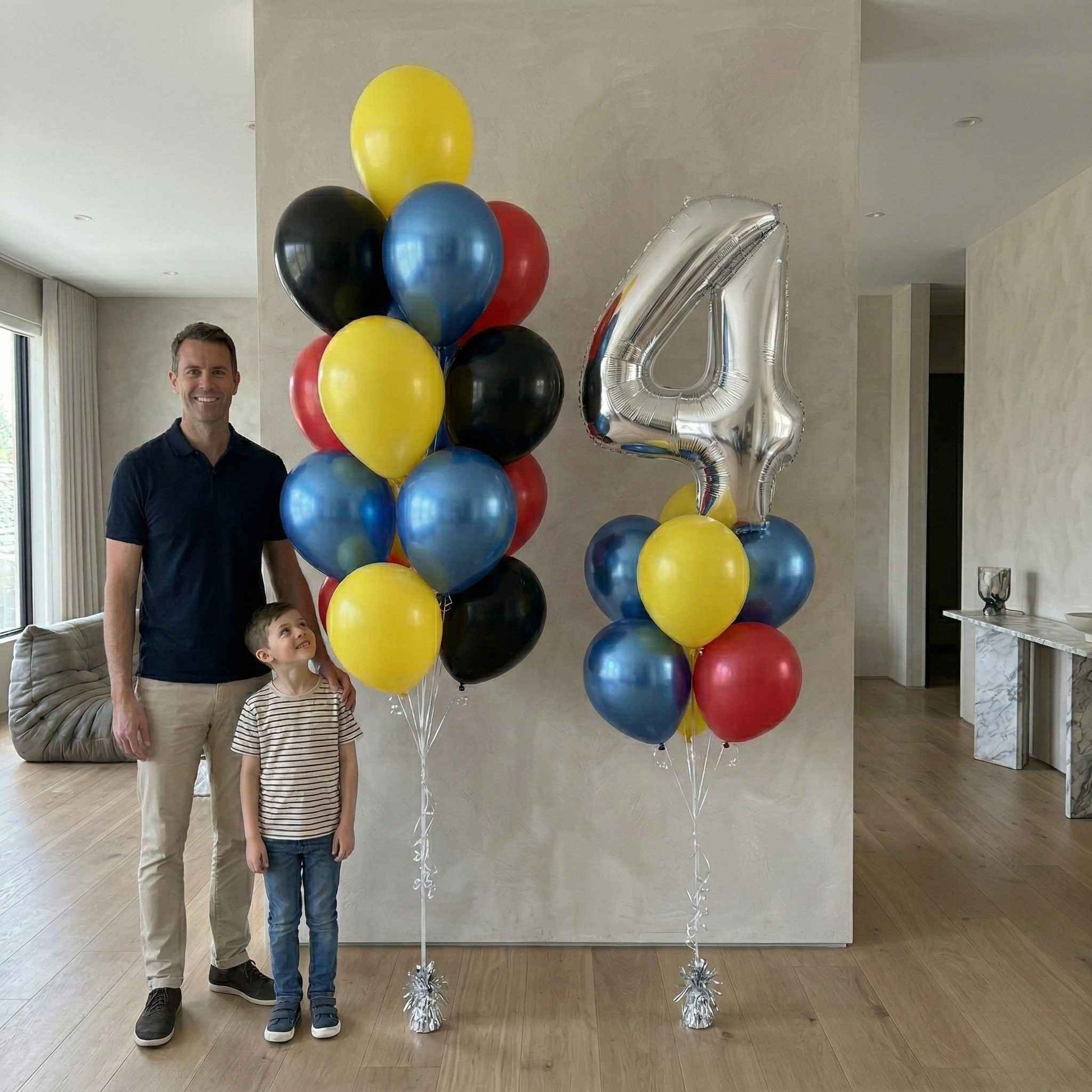Man and child standing next to large colorful balloons with a silver number 4 in a living room.