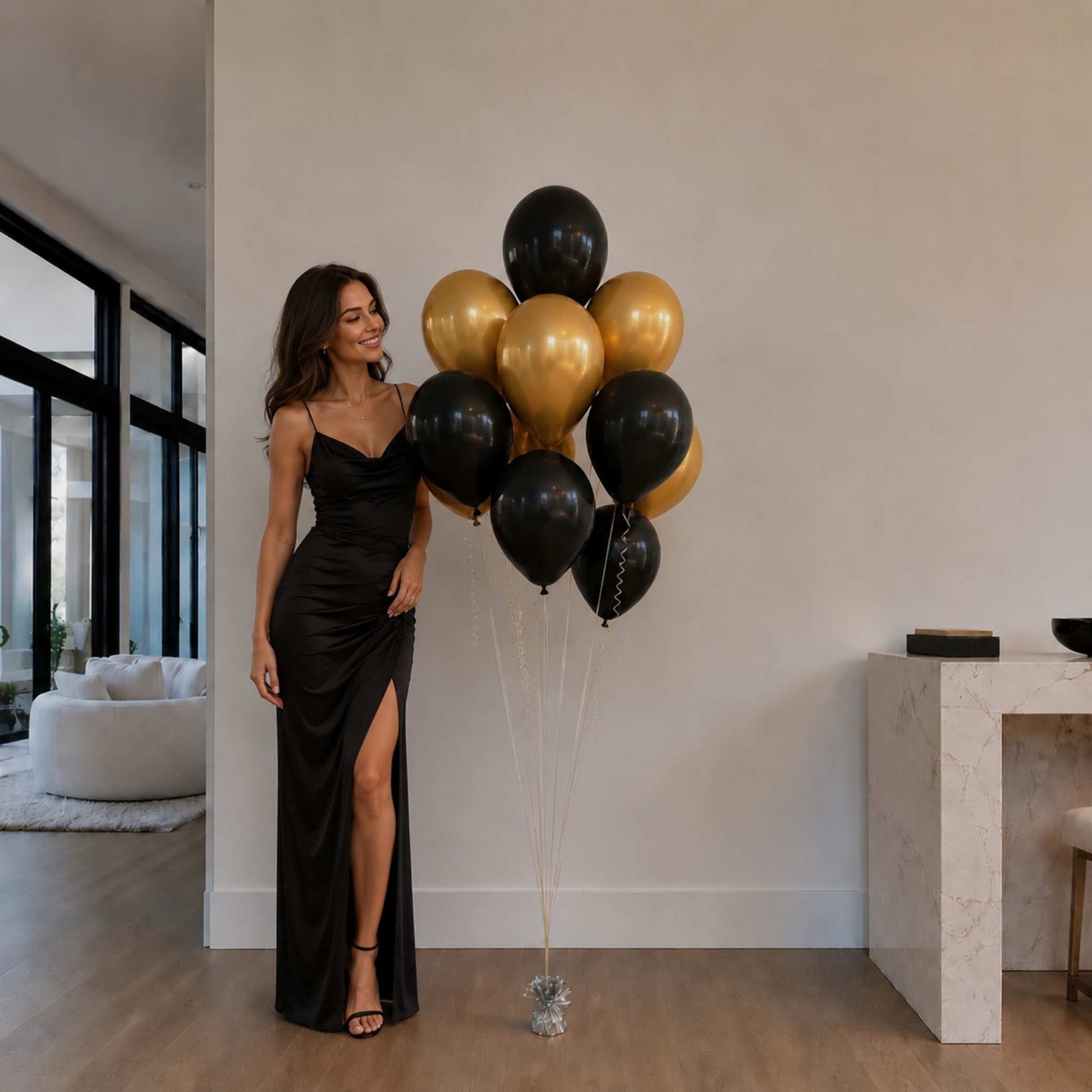 Woman in a black dress holding black and gold balloons in a modern living room.