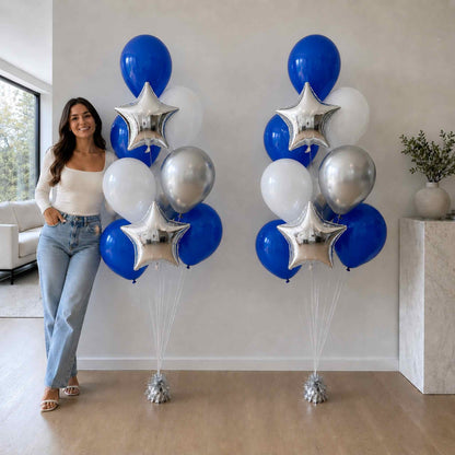 Woman standing next to two large balloon arrangements with blue, silver, and white balloons in a living room.