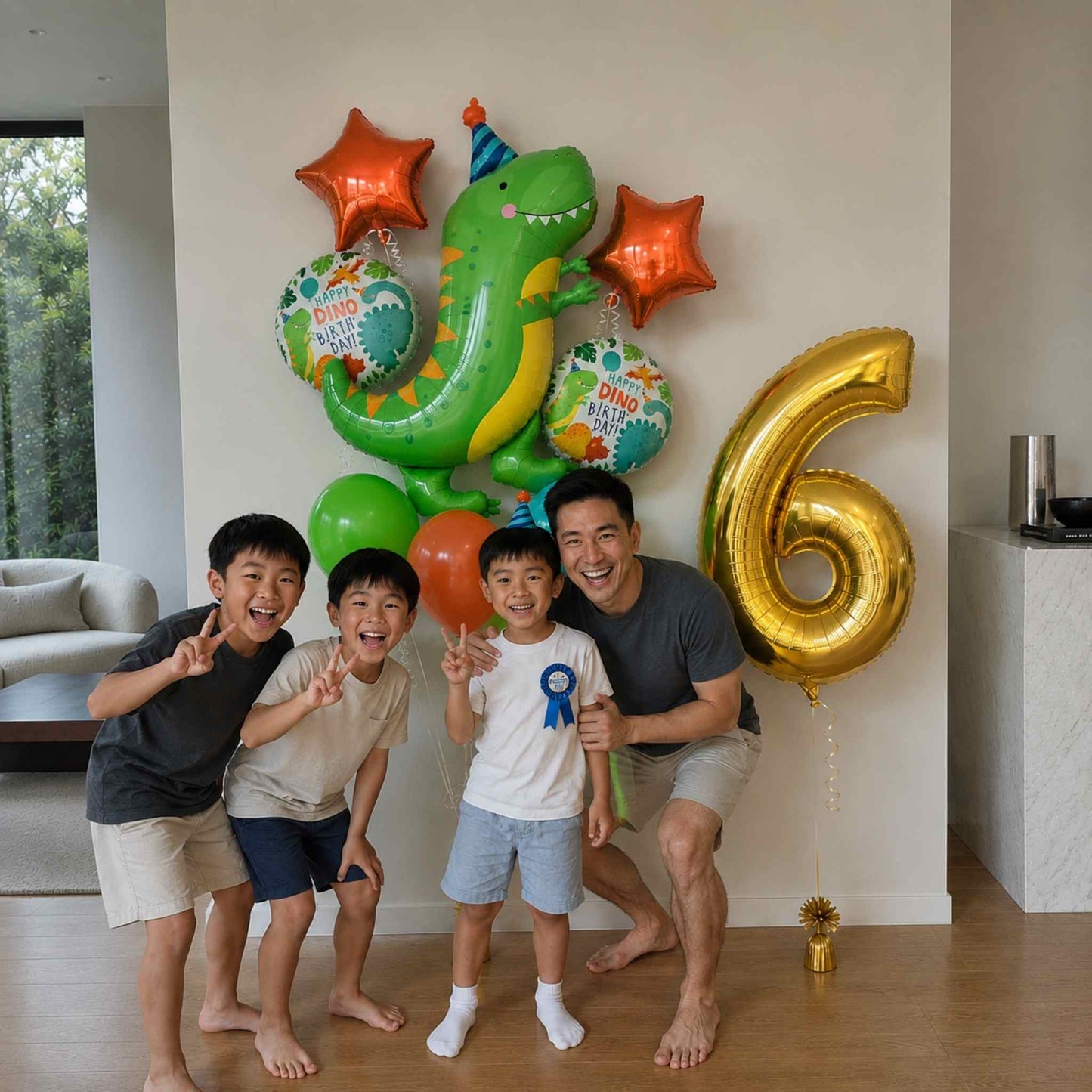 Four people posing with a large green dinosaur balloon, orange star balloons, teal round balloons, and a gold foil balloon shaped like the number 6 in a bright indoor room.