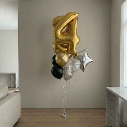 Gold, black, and silver balloons shaped like the number 4 in a living room.