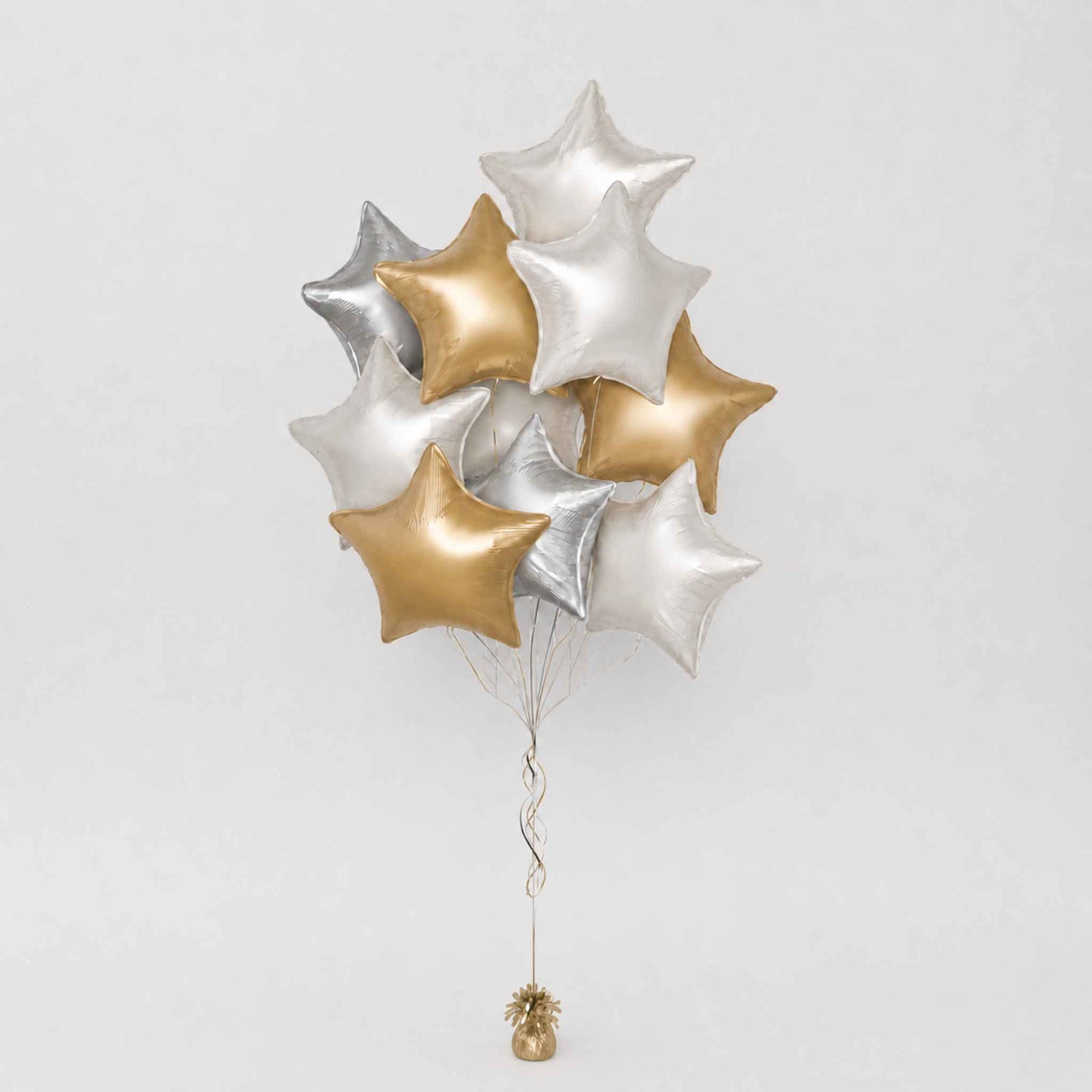 A cluster of metallic star-shaped balloons in silver and gold, tied together with thin strings and a small gold finial at the bottom, photographed against a plain light gray background.