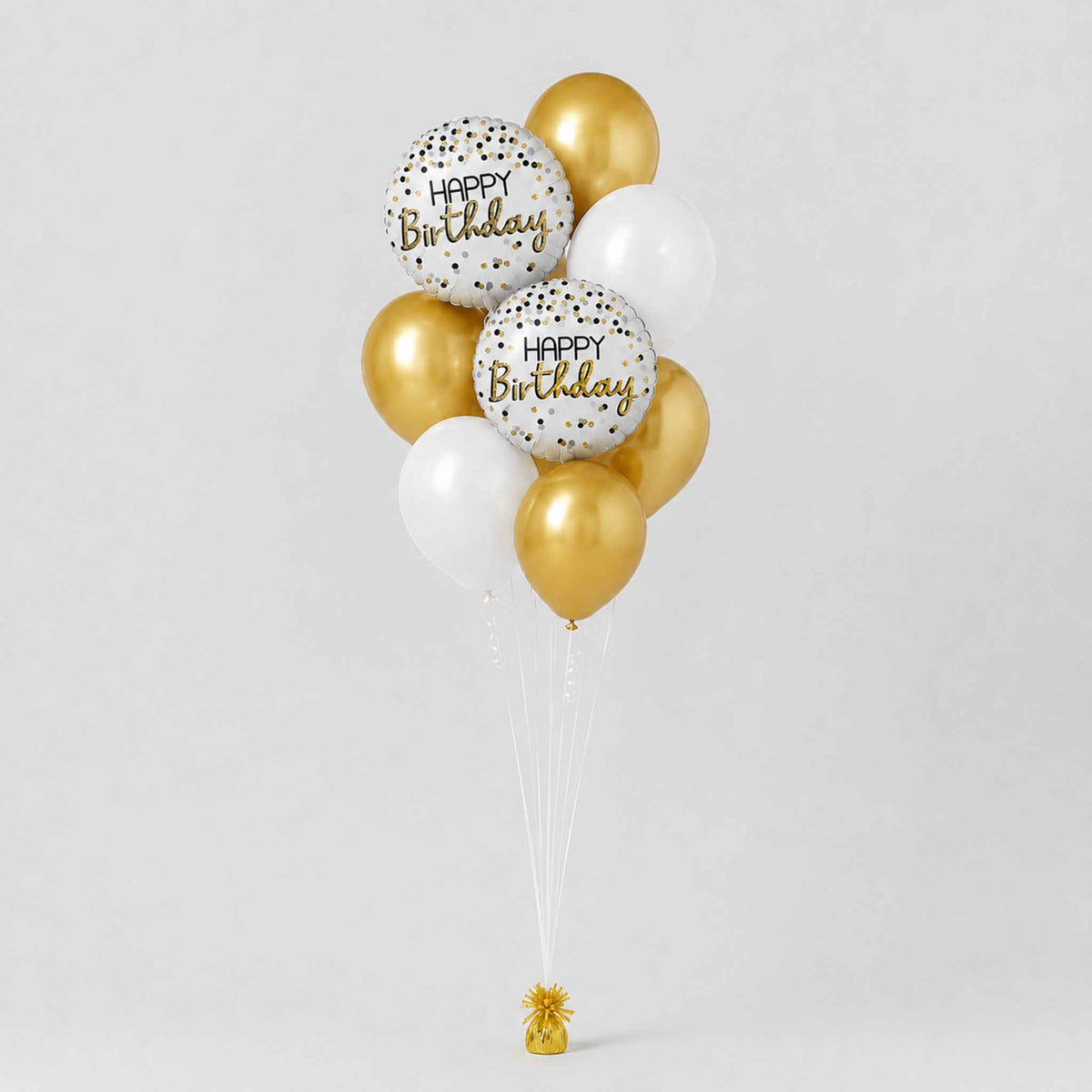 A cluster of metallic gold, white, and clear balloons tied together with white strings, featuring two white balloons printed with 'Happy Birthday' in gold script and gold confetti, on a light gray background.
