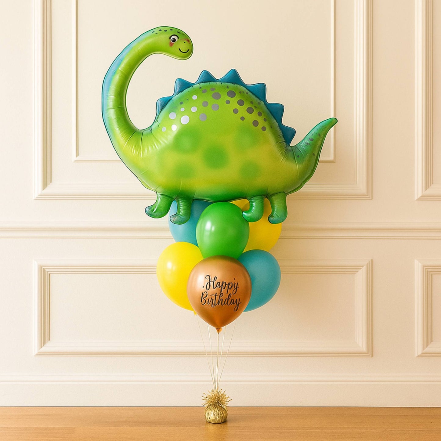 Dinosaur-shaped balloon with smaller balloons and 'Happy Birthday' message against a beige wall.