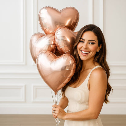 Woman holding rose gold heart-shaped balloons against a white wall