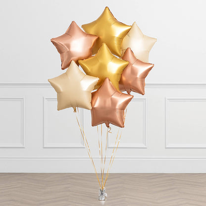 Bouquet of gold, rose gold, and white star-shaped balloons against a white paneled wall.