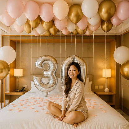 Woman sitting on a bed with balloons and number '3' decoration, likely celebrating a birthday.