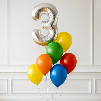 Silver number 3 balloon with colorful balloons against a white wall.