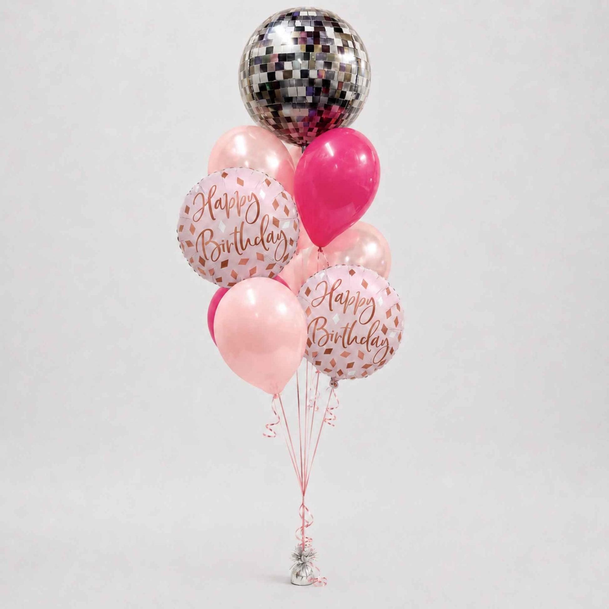 A cluster of birthday balloons on strings, including a large silver disco ball balloon, a bright pink balloon, two pink balloons with rose gold 'Happy Birthday' text, and two clear balloons with pink confetti and 'Happy Birthday' text, set against a light gray background.