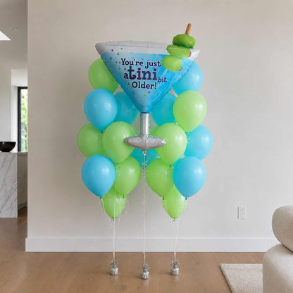 Decorative balloon stand with blue and green balloons and a cocktail glass-shaped balloon in a room.